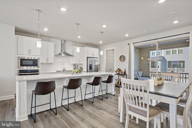 kitchen featuring white cabinetry, stainless steel appliances, a spacious island, decorative light fixtures, and wall chimney exhaust hood