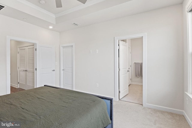 bedroom with connected bathroom, crown molding, light colored carpet, and a raised ceiling