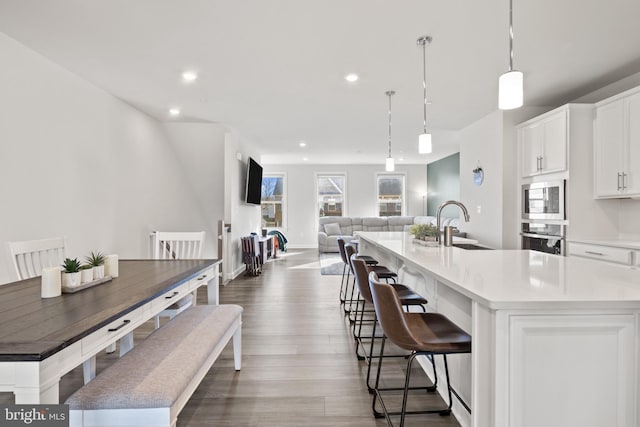 kitchen featuring sink, white cabinetry, decorative light fixtures, a center island with sink, and appliances with stainless steel finishes