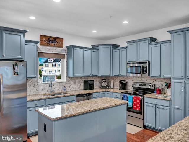 kitchen with sink, appliances with stainless steel finishes, a kitchen island, light hardwood / wood-style floors, and backsplash