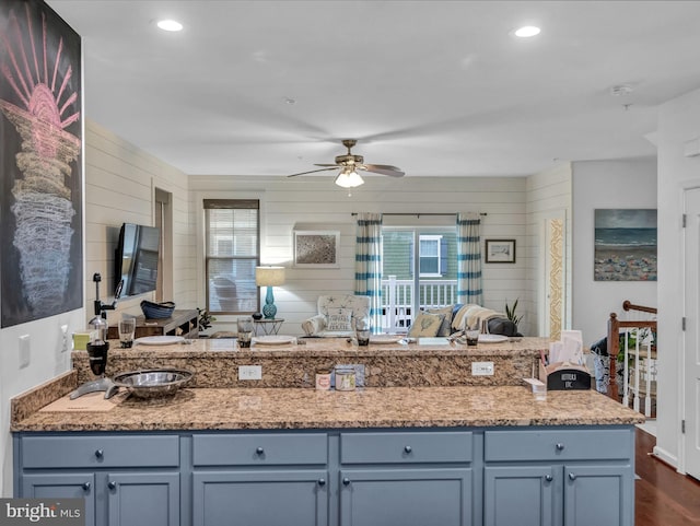 kitchen featuring ceiling fan, light stone countertops, dark hardwood / wood-style floors, and wooden walls