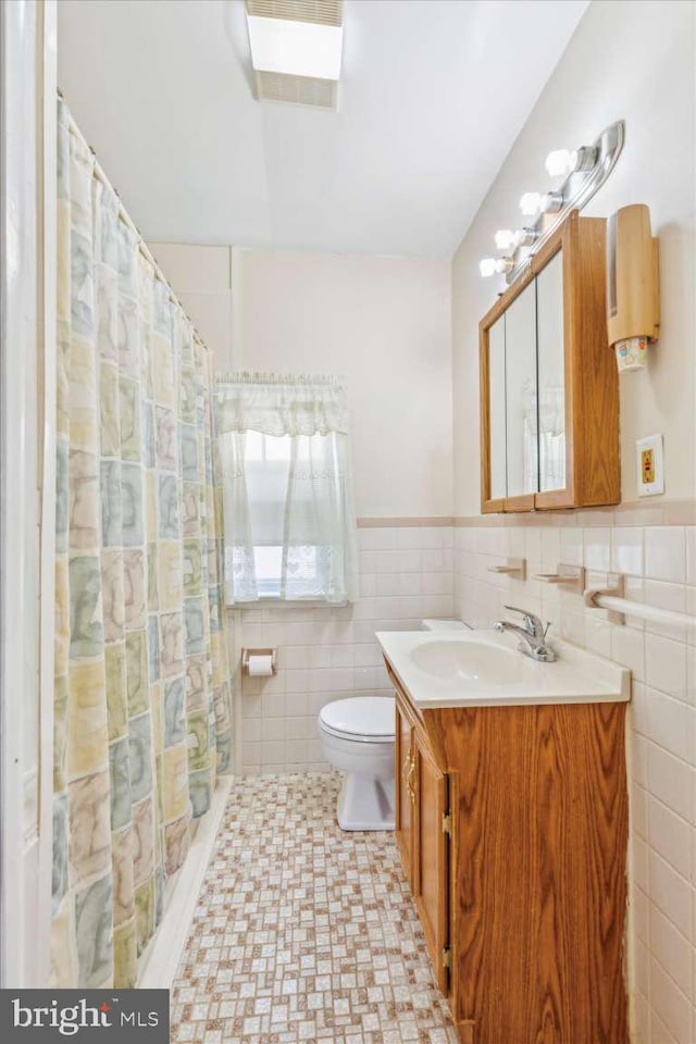 bathroom with walk in shower, vanity, toilet, and tile walls