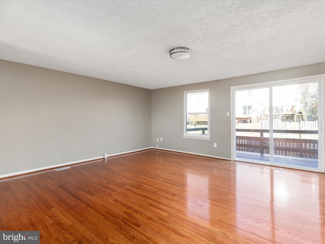 spare room featuring a healthy amount of sunlight, a textured ceiling, and light hardwood / wood-style floors