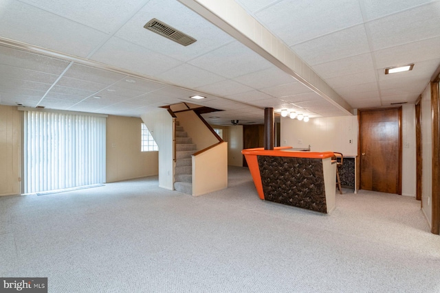 basement with a paneled ceiling, bar, and carpet