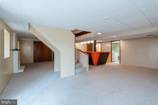 basement with light carpet, washer / clothes dryer, and wooden walls