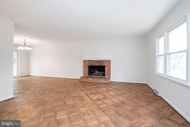 unfurnished living room with light parquet flooring, a fireplace, and a notable chandelier