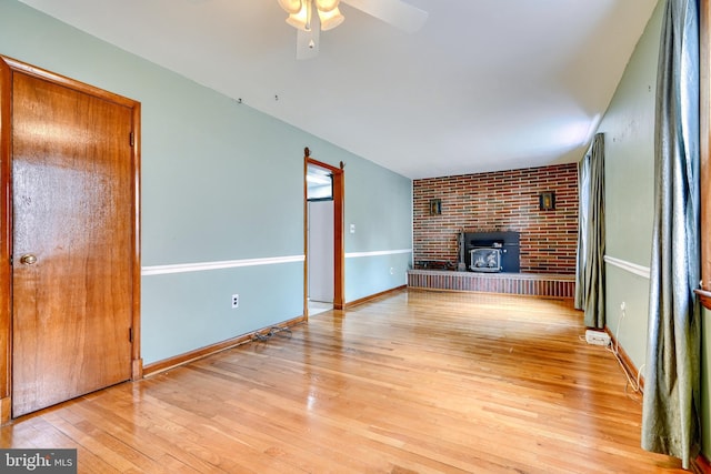 unfurnished living room featuring ceiling fan, a wood stove, and light wood-type flooring