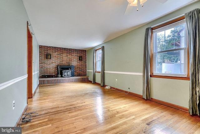 unfurnished living room with ceiling fan, plenty of natural light, light hardwood / wood-style floors, and a wood stove