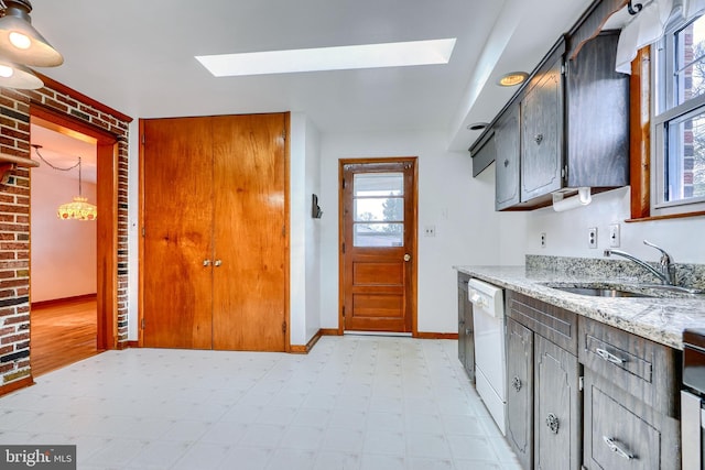 kitchen featuring sink, a skylight, light stone countertops, and dishwasher