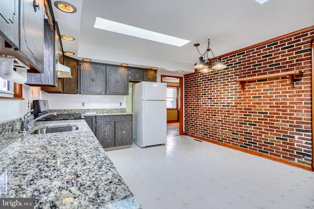 kitchen featuring dark brown cabinetry, sink, a skylight, white refrigerator, and brick wall