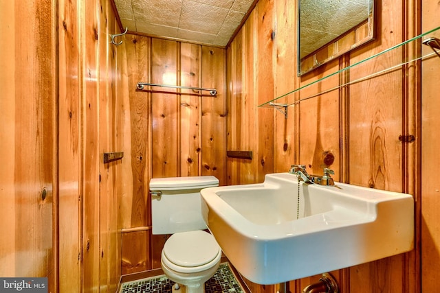 bathroom featuring toilet, sink, and wood walls