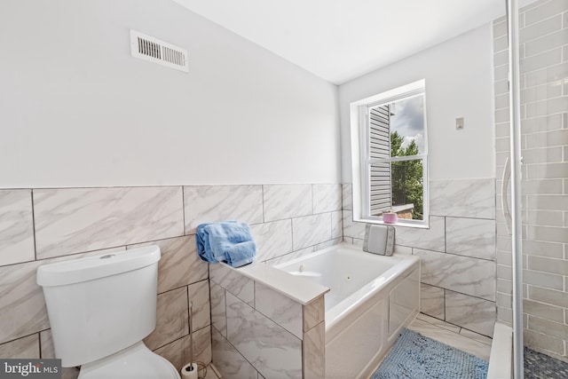 bathroom with tile walls, a bathtub, and toilet