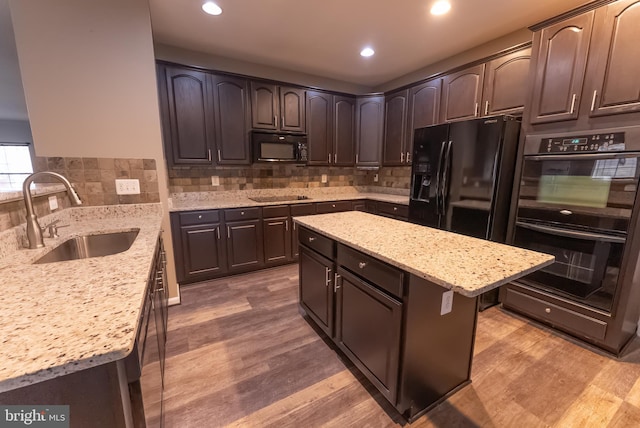 kitchen with sink, dark brown cabinets, a center island, black appliances, and light stone countertops