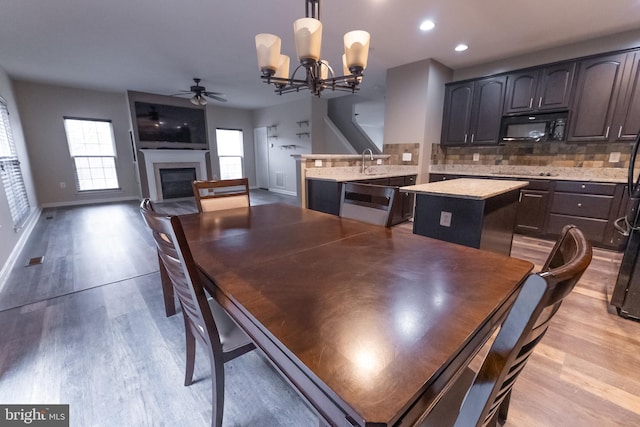 dining space featuring sink, ceiling fan with notable chandelier, and light wood-type flooring