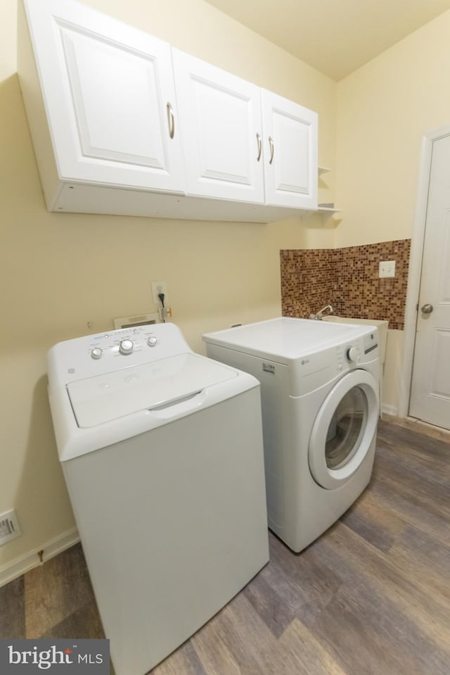 laundry area with wood-type flooring, washing machine and dryer, and cabinets