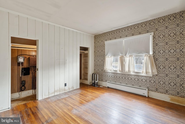 empty room featuring wood-type flooring and a baseboard heating unit