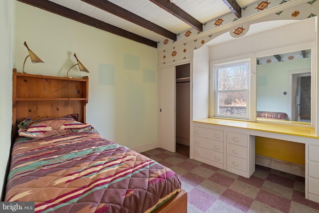 bedroom with beam ceiling, built in desk, and a closet