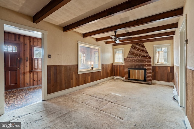 unfurnished living room with ceiling fan, wooden walls, a fireplace, and beam ceiling