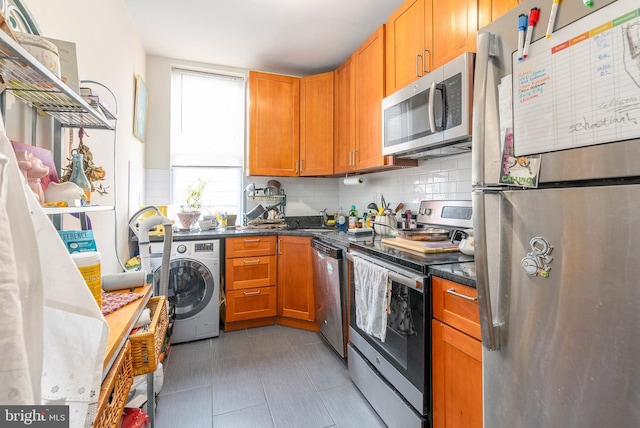 kitchen with stainless steel appliances, washer / clothes dryer, dark tile patterned flooring, and decorative backsplash