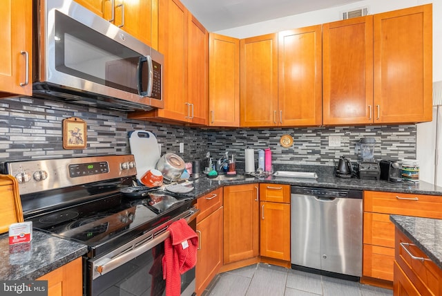 kitchen featuring tasteful backsplash, appliances with stainless steel finishes, light tile patterned floors, and dark stone countertops