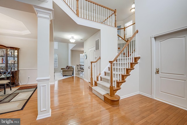 foyer featuring crown molding, a high ceiling, light hardwood / wood-style flooring, and ornate columns