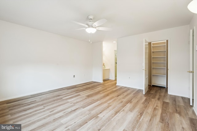 unfurnished bedroom featuring a ceiling fan, ensuite bathroom, a walk in closet, light wood-type flooring, and a closet