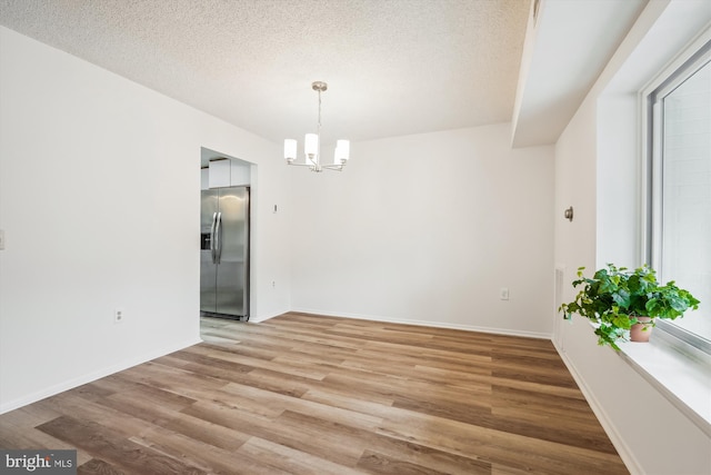 unfurnished dining area featuring a textured ceiling, light wood-type flooring, baseboards, and a notable chandelier