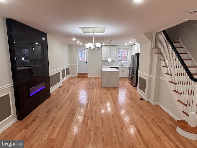 kitchen with stainless steel refrigerator, decorative light fixtures, sink, white cabinets, and light hardwood / wood-style flooring