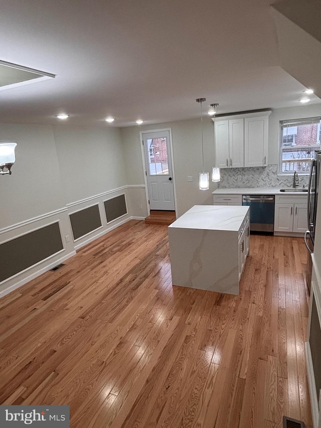 kitchen featuring pendant lighting, white cabinetry, a kitchen island, stainless steel dishwasher, and light wood-type flooring