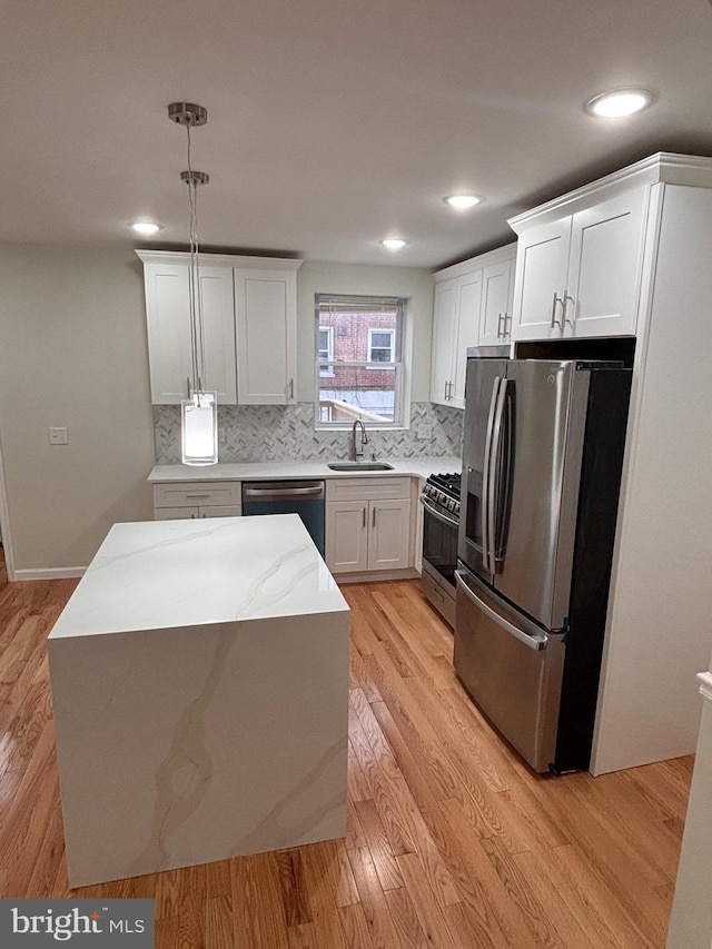 kitchen with appliances with stainless steel finishes, pendant lighting, sink, white cabinets, and light hardwood / wood-style floors