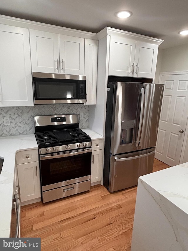 kitchen with backsplash, stainless steel appliances, light stone counters, white cabinets, and light wood-type flooring