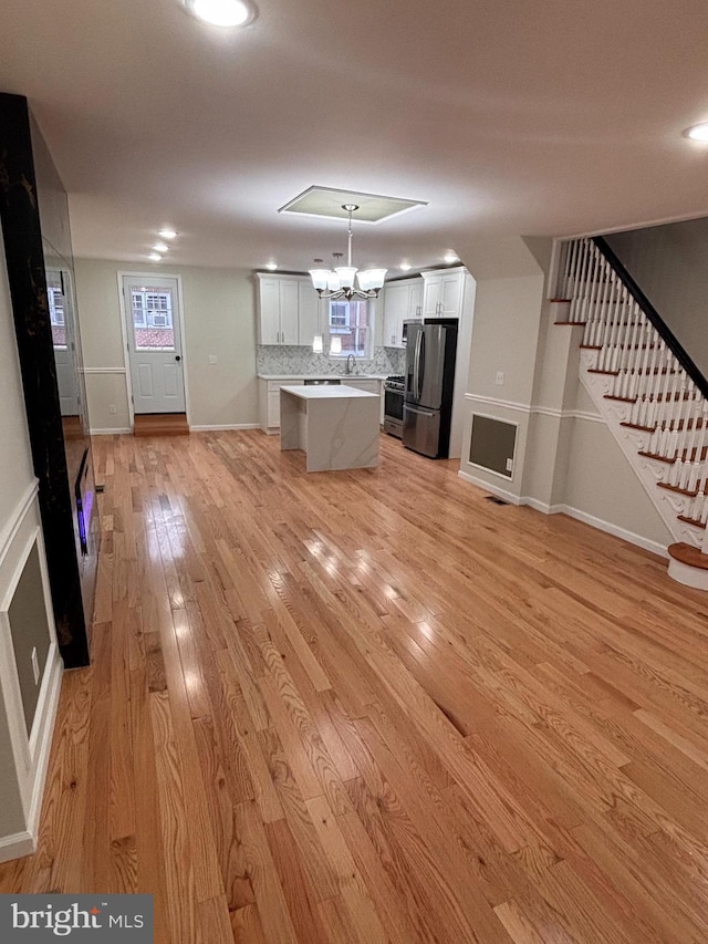 kitchen featuring a kitchen island, decorative light fixtures, decorative backsplash, stainless steel appliances, and light hardwood / wood-style flooring