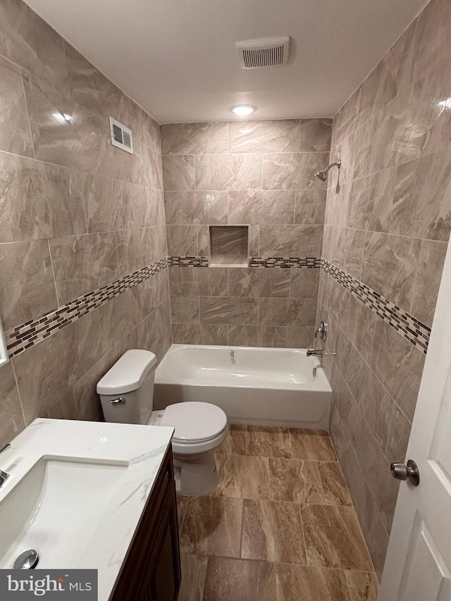 full bathroom featuring tiled shower / bath, tile walls, vanity, and toilet