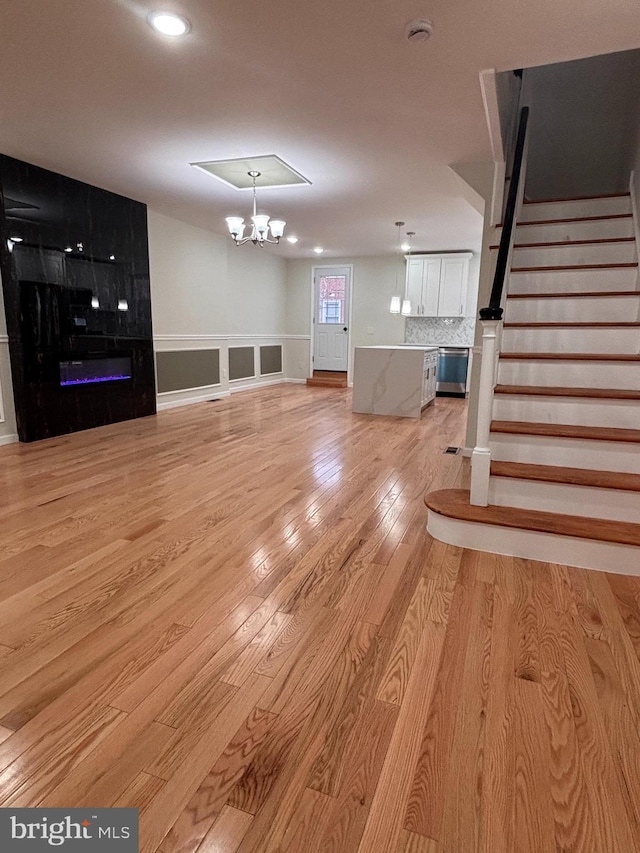 unfurnished living room with a notable chandelier, a fireplace, and light hardwood / wood-style floors