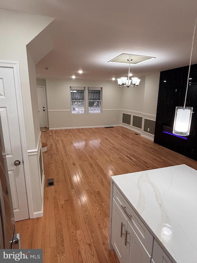 kitchen featuring white cabinets, hanging light fixtures, a notable chandelier, light stone counters, and light hardwood / wood-style floors