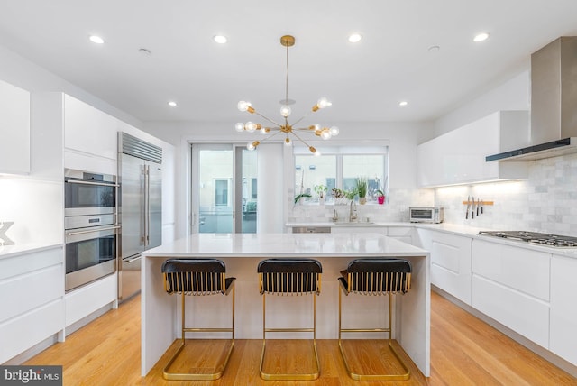 kitchen with wall chimney exhaust hood, sink, a center island, stainless steel appliances, and white cabinets