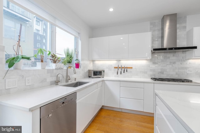 kitchen featuring appliances with stainless steel finishes, white cabinetry, sink, light hardwood / wood-style floors, and wall chimney exhaust hood