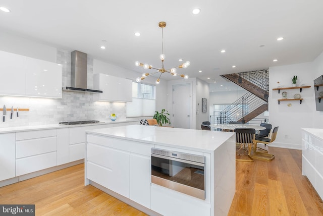 kitchen with white cabinets, hanging light fixtures, a center island, stainless steel appliances, and wall chimney range hood