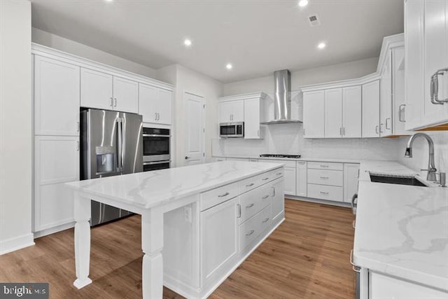 kitchen with sink, white cabinetry, a kitchen island, stainless steel appliances, and wall chimney range hood