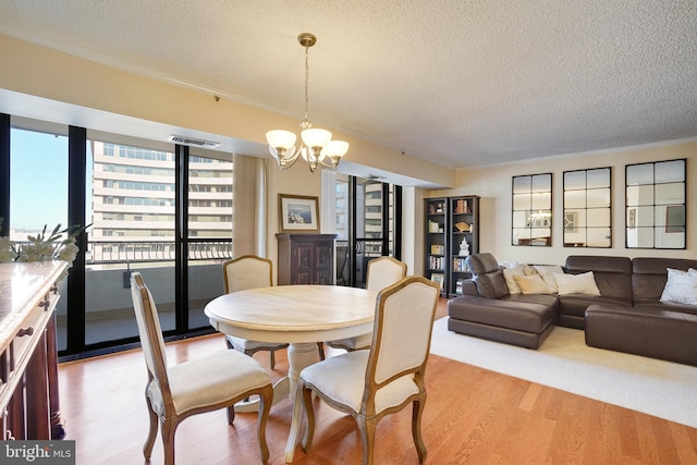 dining room with ornamental molding, a textured ceiling, an inviting chandelier, and light hardwood / wood-style flooring