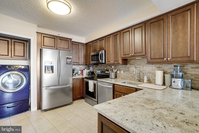 kitchen featuring sink, stainless steel appliances, light stone counters, tasteful backsplash, and washer / dryer