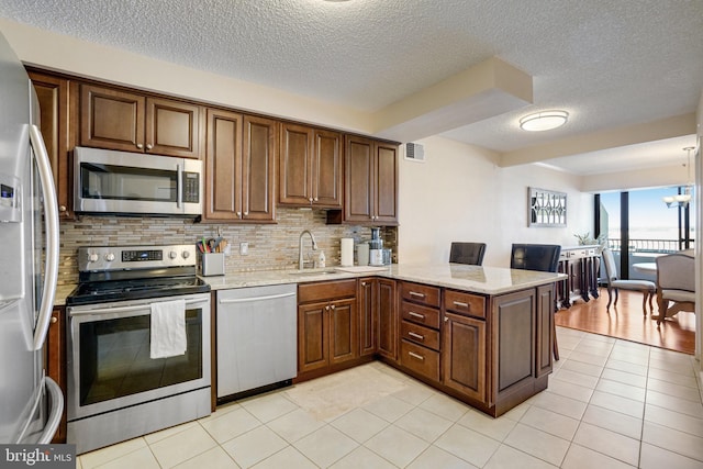 kitchen featuring sink, stainless steel appliances, tasteful backsplash, light tile patterned flooring, and kitchen peninsula