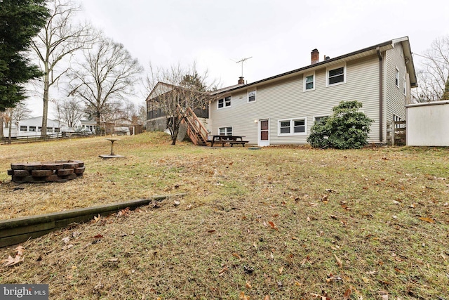 back of property with an outdoor fire pit and a lawn