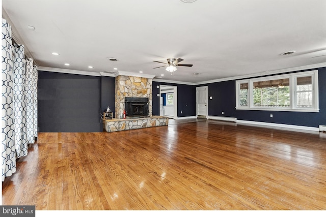 unfurnished living room with baseboard heating, plenty of natural light, a stone fireplace, and wood-type flooring