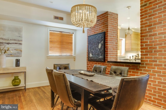 dining room with an inviting chandelier, light hardwood / wood-style floors, and brick wall