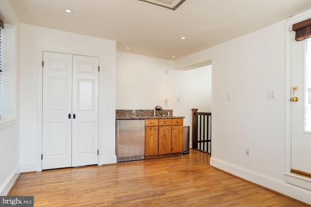 bar featuring sink, dark stone counters, stainless steel refrigerator, and light hardwood / wood-style floors