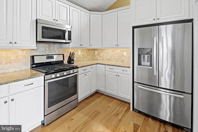 kitchen with white cabinetry, decorative backsplash, light stone counters, stainless steel appliances, and light wood-type flooring