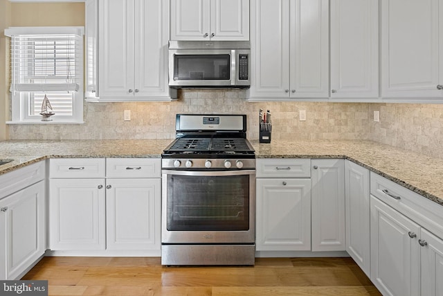 kitchen with white cabinetry, light stone countertops, stainless steel appliances, and light wood-type flooring