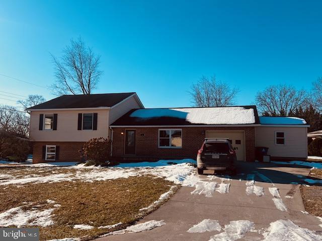 snow covered house with brick siding, driveway, and an attached garage