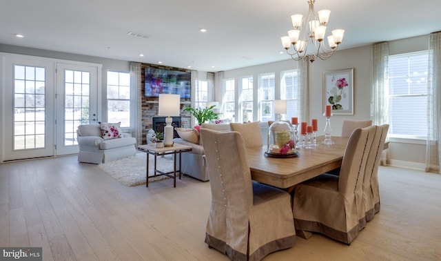 dining space featuring plenty of natural light, an inviting chandelier, a fireplace, and light wood-type flooring